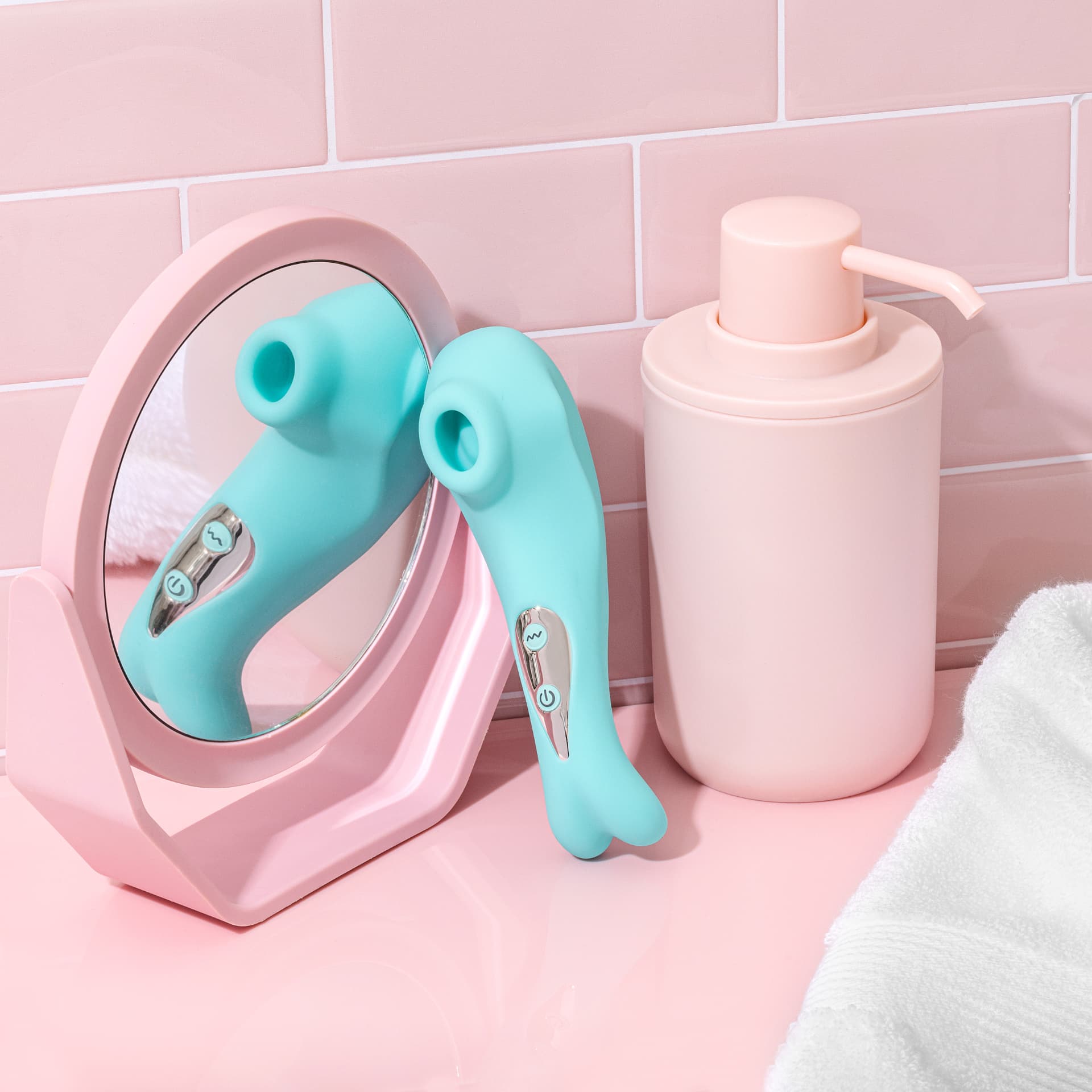 Mint green suction stimulator resting against a pink vanity mirror beside a soap dispenser and white towel